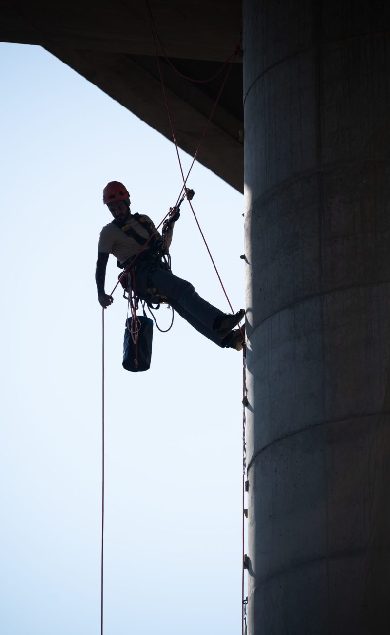 Industrial climber checking the security on concrete bridge pillar using rope access techniques