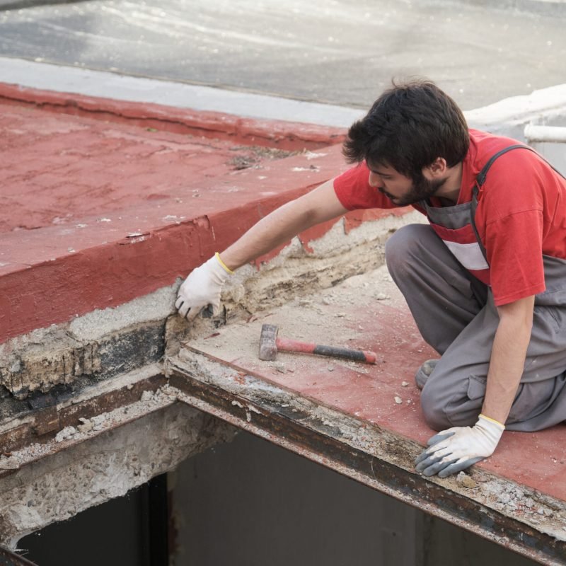 Young man tearing the roof of a house down using a mallet.